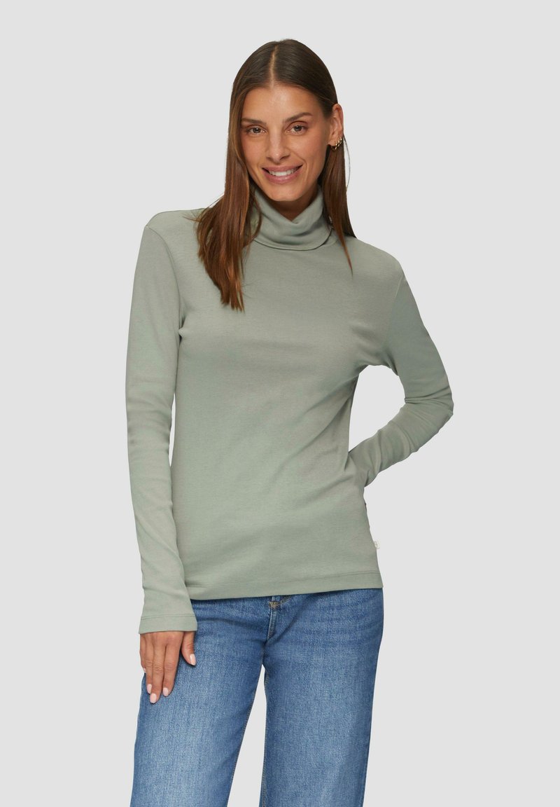 Jasnozielony golf z długim rękawem, wykonany z gładkiego materiału, w połączeniu z niebieskimi dżinsami. Charakteryzuje się dopasowanym krojem i wysokim dekoltem.