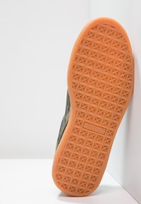 Sulan på en sneaker med en orange gummiyttersula som har ett stjärnmönstrat mönster och en synlig Puma-logotyp i mitten.