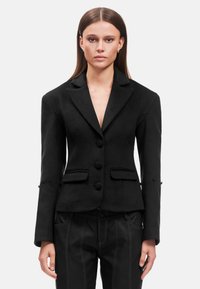 Blazer nero su misura realizzato in tessuto testurizzato, con revers a punta, chiusura a doppio bottone e tasche a patta. Vestibilità slim con maniche lunghe.