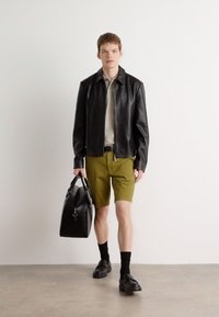 Svart lær zip-up jakke, lysegrønn poloskjorte, olivenfargede shorts, svart veske, svarte sokker og robuste sko. Enkelt, skreddersydd design.