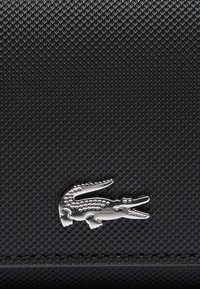 Matériau noir texturé avec un logo en forme de crocodile argenté dans le coin inférieur, mettant en avant une surface lisse et un gravure détaillée.