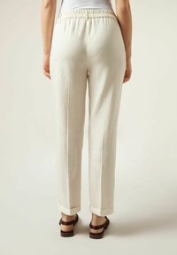 Ljusbeige linnebyxor med elastisk midja, raka ben och uppvikta fållar. Bärs med bruna sandaletter med remmar.