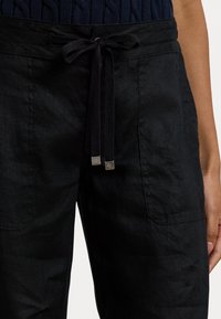 Black linen pants with a drawstring waist, featuring metal accents on the drawstrings and two side pockets. Textured fabric finish.