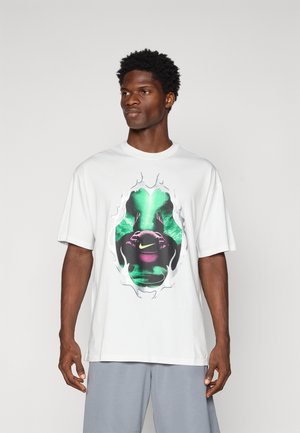 Hvid bomulds-T-shirt med et farverigt grafisk design i sort og grønne nuancer, fremhævet af et Nike-logo. Korte ærmer, afslappet pasform.