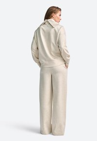 Set de loungewear bej, alcătuit dintr-un hanorac cu croială relaxată și geci cu pantaloni largi. Material moale, texturat și detalii de design subtile.