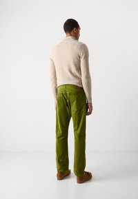 Beige sweater og grønne fløjlsbukser. Bukserne har baglommer og en læderlap. Brune sko supplerer outfittet.
