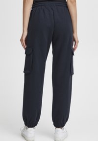 Navyblauwe cargobroek met een elastische tailleband, twee zijzakken met kleppen en elastische boorden bij de enkels. Klassieke katoenen mix stof.