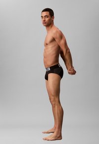 Slip neri in cotone con cintura logo, caratterizzati da una vestibilità aderente e una texture liscia, indossati da un modello in posa di profilo.