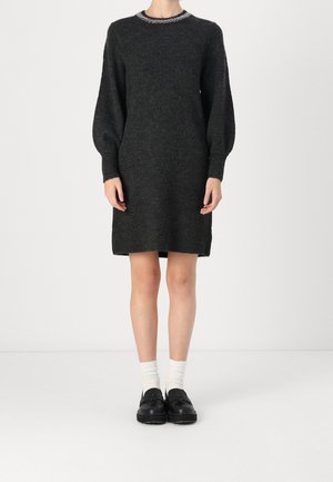 Robe en maille gris foncé longueur genou avec manches ballon longues, encolure ronde ornée, portée avec des chaussettes blanches et des mocassins noirs.