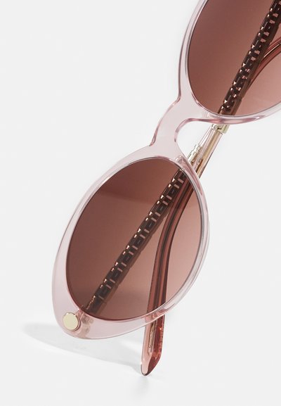 Pink tinted sunglasses with oval lenses, transparent frames, and a textured brown hinge detail. Gold accent on frame.