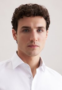 Witte shirt met een gestructureerde kraag, voorzien van een patroon in de binnenkraag. De stof lijkt glad en lichtjes gestructureerd.