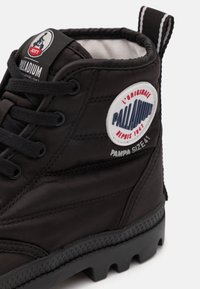 Stivale alla caviglia nero realizzato in materiale texturizzato, con una toppa rotonda con logo, lacci neri e suola robusta con battistrada prominente.