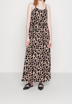 Kvinde iført en ærmeløs, beige og sort leopardprint maxikjole med tynde stropper og sorte spidse flade sko.