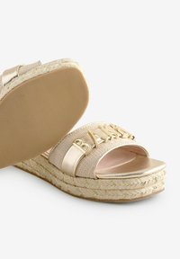 Gouden espadrille sandalen met platte zool, met geweven stoffe banden en een merknaam die in gouden letters is benadrukt. Rubberen zoolstructuur.