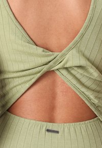 Olivenfarget ribbet topp med en dyp V-rygdesign, som har en vridd detalj bak. Stoffet er mykt, med en tett passform.