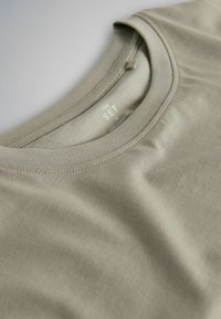 T-shirt vert olive clair à col rond, en tissu doux, taille moyenne, avec des coutures plates nettes autour du col.