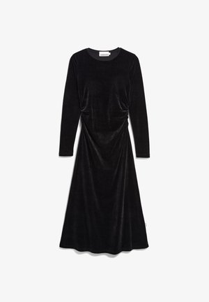 Schwarzes Samtkleid mit langen Ärmeln und Rundhalsausschnitt, das mit gerafften Details an der Taille und einem fließenden Rock bis zur Hälfte der Wade versehen ist.