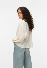 Ljus krämfärgad skjorta med lång ärm och strukturerat mönster, lös passform och vida ärmar, kombinerat med ljusblå högmidjade jeans.