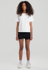 White cotton t-shirt with "SUMMER ESCAPE" text, paired with black denim shorts. Worn with white sneakers and striped blue and white socks.