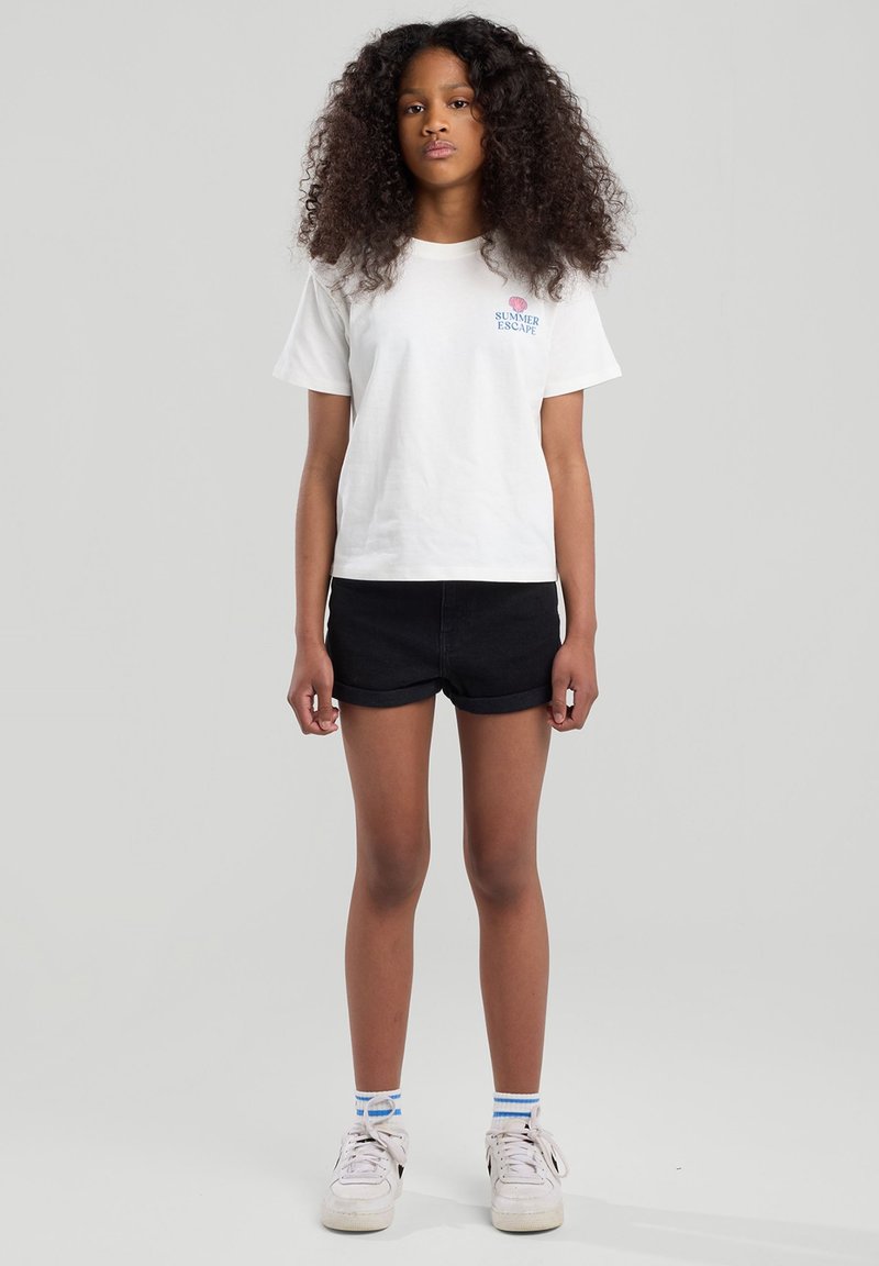 White cotton t-shirt with "SUMMER ESCAPE" text, paired with black denim shorts. Worn with white sneakers and striped blue and white socks.