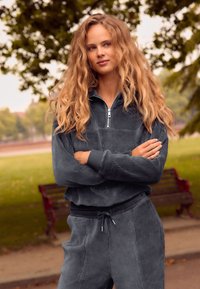 Ensemble en velours côtelé gris comprenant un haut zippé avec une poche frontale, une taille élastique et un pantalon assorti avec des ourlets resserrés.
