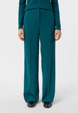 Spodnie o szerokich nogawkach w kolorze morskim z gładkiego materiału, z płaskim przodem i subtelnymi szlufkami na pasek. W połączeniu z czarnymi butami.