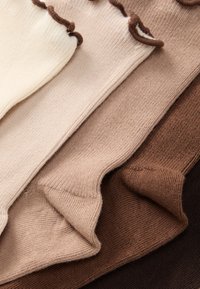 Fire par sokker i forskellige nuancer: elfenben, lys beige, medium beige og mørkebrun. Struktureret strik med bølgede kanter øverst.