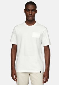 White cotton t-shirt with a round neckline, short sleeves, and a chest pocket. Features a textured finish and subtle brand label on the hem.