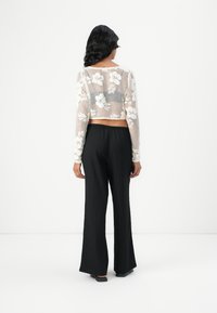 Transparante, witte, langemouwen crop top met bloemenbroderie, gecombineerd met hoge, zwarte, gestructureerde wijde broek.