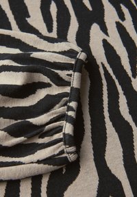 Zebra-Print-Stoff mit kräftigen schwarz- und cremefarbenen Streifen sowie einer strukturierten Strickoberfläche. Auffällige Rüschendetails entlang des Randes.