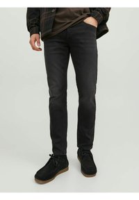 Jeans neri slim fit con una texture morbida, caratterizzati da un design a cinque tasche. Abbinati a scarpe in suede nere e una camicia a quadri indossata sopra un top scuro.