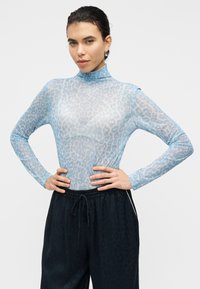 Ανοιχτό μπλε διάφανο τοπ με μακριά μανίκια, σχέδιο με μοτίβο λεοπάρδαλης, ψηλό γιακά και εφαρμοστή γραμμή, συνδυασμένο με σκούρο παντελόνι jogger.