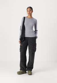 Un haut gris côtelé à manches longues associé à un pantalon cargo foncé et duveteux avec des poches à rabat. Des chaussures chunky vert olive complètent la tenue.