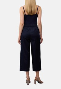 Marinefarbene Cropped-Hosen mit elastischem Bund, kombiniert mit einem figurbetonten marineblauen Tanktop. Das Outfit wird durch beigefarbene High-Heel-Sandalen ergänzt.