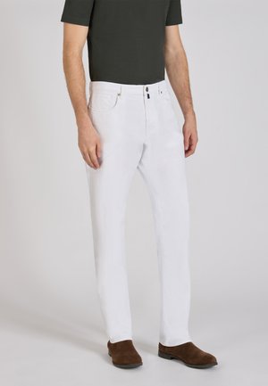 Witte katoenen broek met een recht model, vijf zakken en een messing knoopsluiting, gecombineerd met bruine suède schoenen.