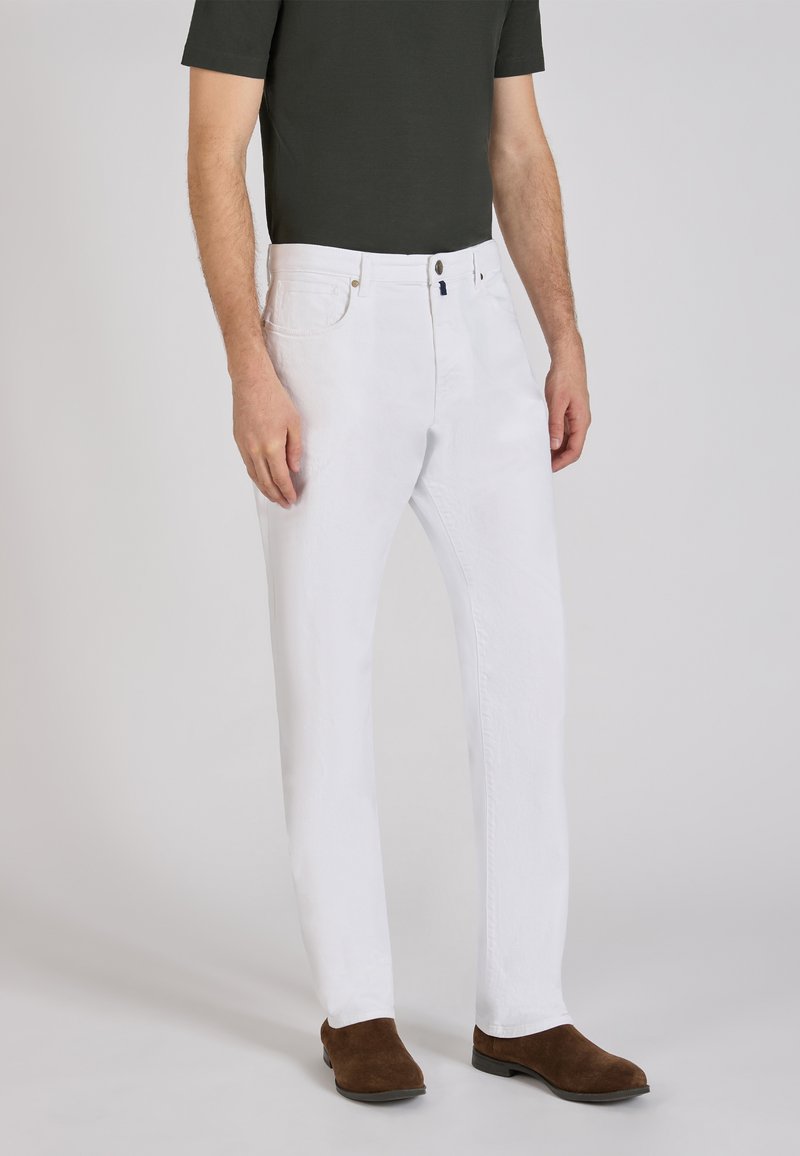 Pantalones de algodón blancos con un diseño de pierna recta, cinco bolsillos y cierre de botón de latón, combinados con zapatos de ante marrones.