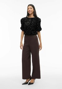 Melns top ar spīguļotiem īsiem piedurknēm ar pūkainiem volāniem, kombinēts ar augsta vidukļa, platu brūnu biksēm un melnām, smailām augstpapēžu kurpēm.