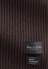 Bruine geribbelde kasjmiergeweven stof met twee zwarte labels; één met "Marc O'Polo" en de andere met de tekst "gemaakt van 100% goede kasjmier."