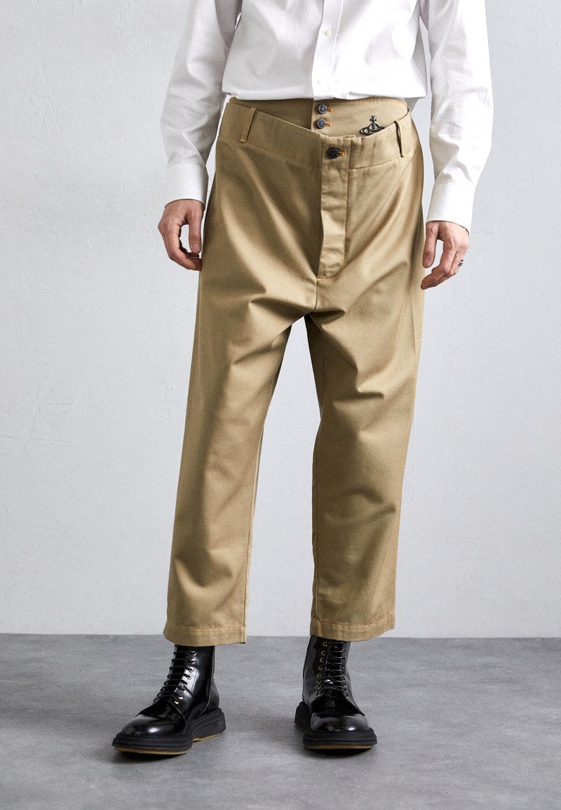 Beige, hochtaillierte Hose mit geknöpftem Vorderteil, flachen Taschen und einem leicht lockeren Schnitt. Kombiniert mit schwarzen Schnürstiefeln.