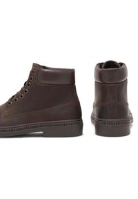 Hnedé kožené členkové topánky s okrúhlym špičkou, šiestimi dierkami, polstrovaným golierom, štruktúrovanou gumovou podrážkou a kontrastnými švami.