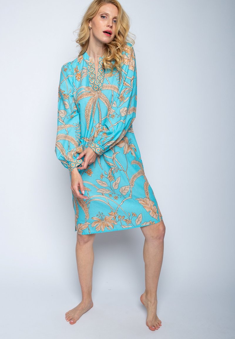 Ein türkisfarbenes Kleid mit einem blumen- und blättermuster in Beige, langen Ballonärmeln und einem runden Ausschnitt mit dekorativem Besatz.