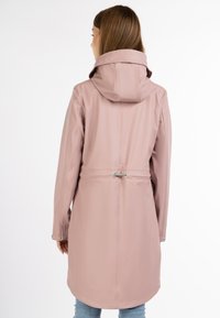 Pink vandtæt regnfrakke med hætte, der har en indsnævret talje, lange ærmer og knappede manchetter. Glat tekstur og minimalistisk design.