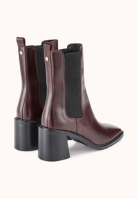 Paire de bottines en cuir marron foncé avec panneaux latéraux élastiques noirs et talons hauts épais sur un fond clair uni.