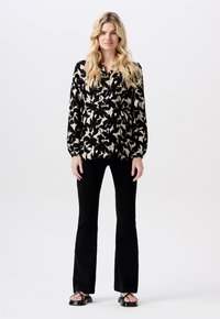 Czarna i beżowa kwiatowa bluzka z długimi rękawami, zapinana na guziki z przodu, w luźnym kroju, zestawiona z czarnymi spodniami dzwonami i sandałami.