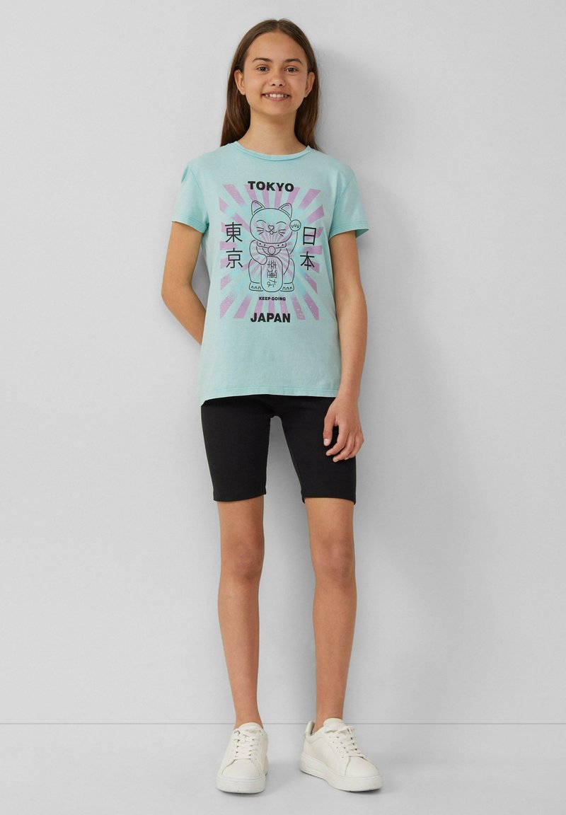 Lichtblauwe t-shirt met korte mouwen en grafische print met een beer en tekst. Gecombineerd met zwarte fietsbroek en witte sneakers.