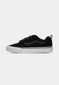 Svart sneakers med polstret krage, teksturert stoff, hvit gummisåle og flate svarte snor. Har en logo på siden og en løfteløkke bakerst.