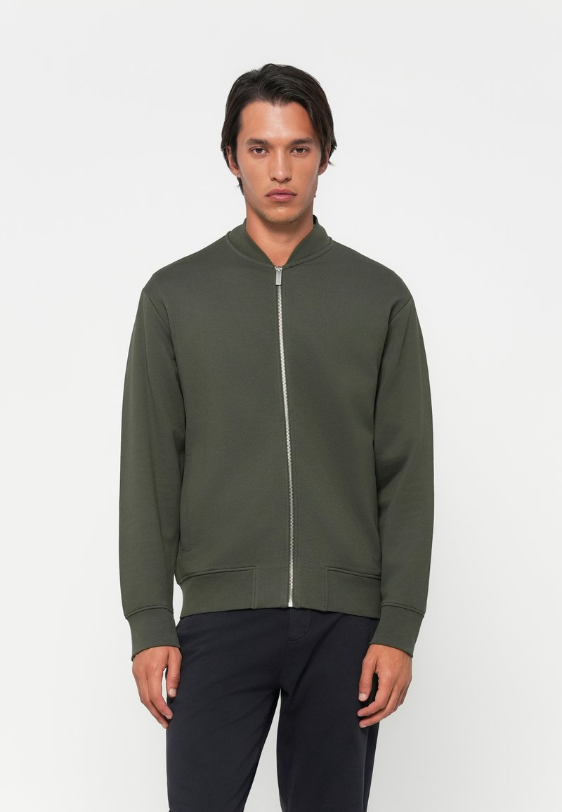 Oliven grøn zip-up sweatshirt med høj krave, ribbede cuffs og kant. Har et enkelt design og glat tekstur.