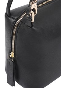 Zwarte leren handtas met een goudkleurige rits, gestructureerd oppervlak, zijlusdetail en een afneembare leren label. Compact en gestructureerd ontwerp.