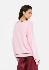 Helles rosa Sweatshirt mit lockerer Passform, schwarzem Streifen an der Ausschnittkante und goldenen Knopf-Akzenten an den Ärmelsäumen.