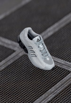 Light gray athletic shoe with mesh upper, three black stripes, rounded toe, and cushioned black sole. Features lacing and logo on tongue.